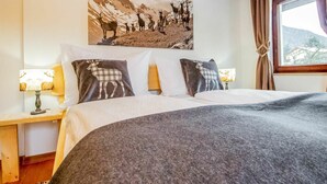 Une chambre avec un grand lit, deux tables de chevet avec des lampes, un tableau représentant un paysage de montagne accroché au mur et une fenêtre avec des rideaux.