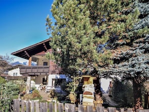 A chalet with a wooden deck, a stone staircase, and a mountain backdrop.