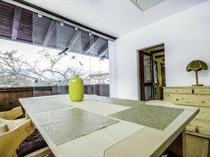 A room with a large table, chairs, a green vase, and a view of trees and buildings outside.