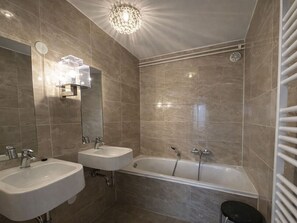 Un baño con dos lavamanos, una bañera, una ducha, un candelabro y un perchero para toallas.