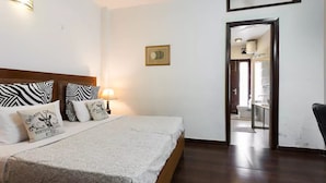 A hotel room with a bed, pillows, a nightstand, a lamp, and a framed picture on the wall. - Perch Arbor Suites (Gurugram)