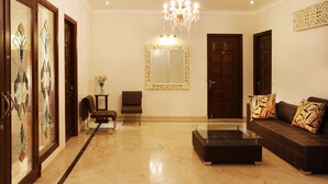 A spacious living room with a chandelier, a sofa, a coffee table, and a large mirror. - Perch Arbor Suites (Gurugram)