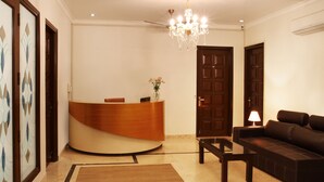 A reception area with a curved wooden desk, a black leather sofa, a chandelier, and a lamp. - Perch Arbor Suites (Gurugram)