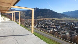 Un edifici modern amb estructura de fusta i un passeig pavimentat amb vista a una vila i muntanyes.