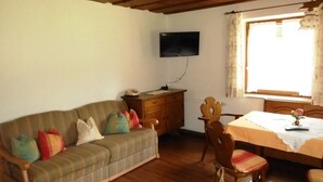 Une pièce chaleureuse avec un canapé, une table à manger en bois et un téléviseur fixé au mur.