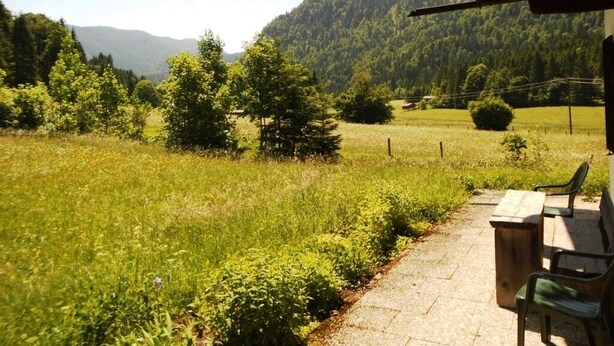 Un espace extérieur aménagé avec des sièges, offrant une vue sur un champ verdoyant et des collines boisées.