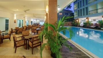 A hotel lobby with a pool, dining area, and a large pillar.