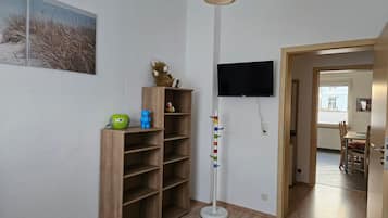 Ett rum med en bokhylla i trä, en tv som är monterad på väggen och en dörr som leder till ett annat rum.