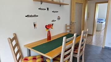 Un comedor con mesa de madera, cojines escoceses y un jarrón con flores. Hay etiquetas en la pared para distintos tipos de café.