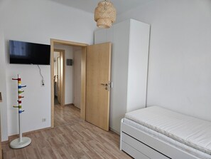 A bedroom with a bed, a television mounted on the wall, a door leading to another room, and a floor lamp.