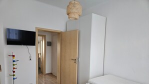 Un dormitorio con cama, televisión montada en la pared, una puerta que da a otra habitación y una lámpara de pie.