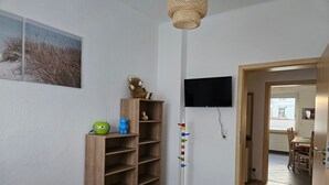 Una habitación con una estantería de madera, un televisor colgado en la pared y una puerta que da a otra estancia.