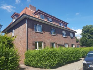 Ein zweistöckiges Backsteingebäude mit zahlreichen Fenstern, einer sichtbaren Tür und einem geparkten Auto davor.