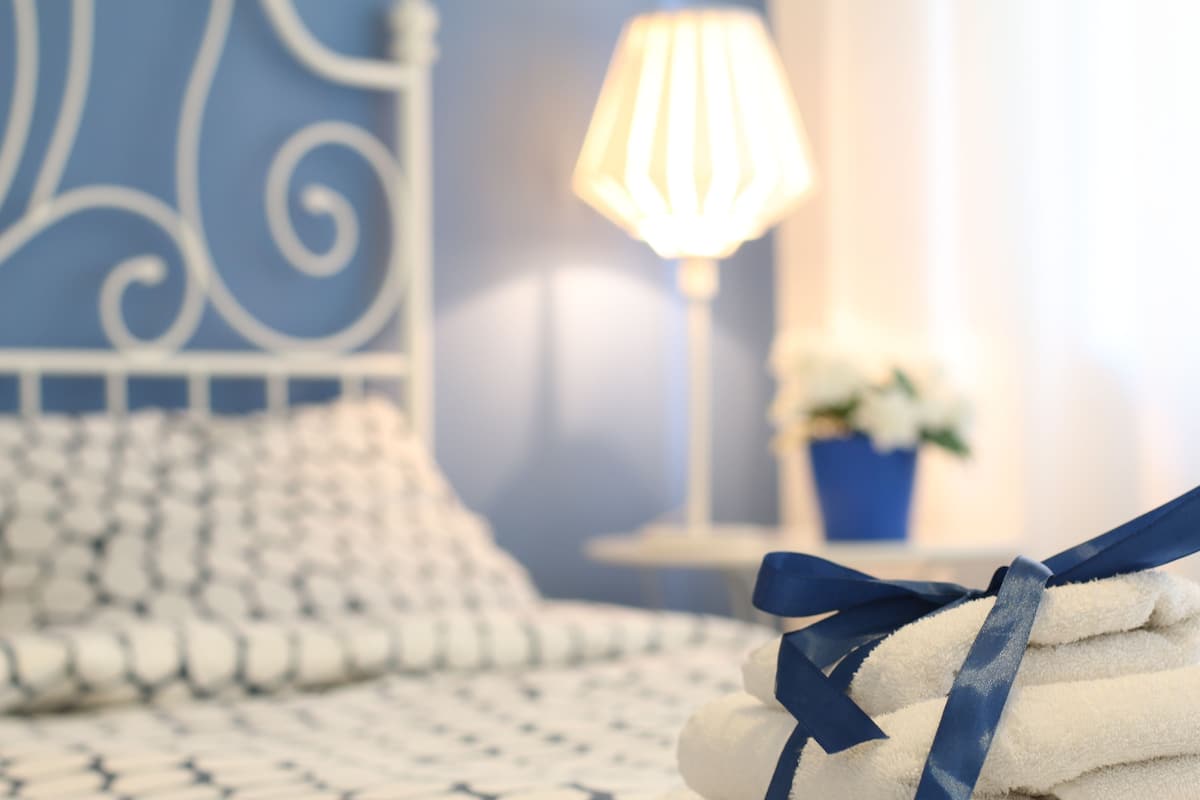 A neatly made bed with a blue headboard, a bedside lamp, and a small table with a blue vase.