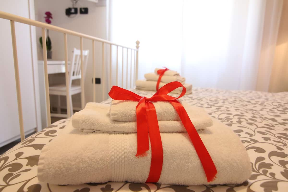 A neatly arranged stack of white towels with red ribbons tied around them on a bed with a patterned bedspread.