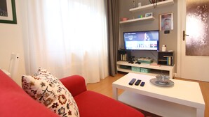 A living room with a red sofa, a white coffee table, and a television on a stand. - Sette sorelle b&b (Cosenza)