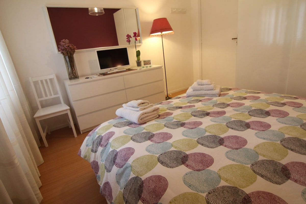 A bedroom with a bed, a desk, a chair, a lamp, and a wardrobe.