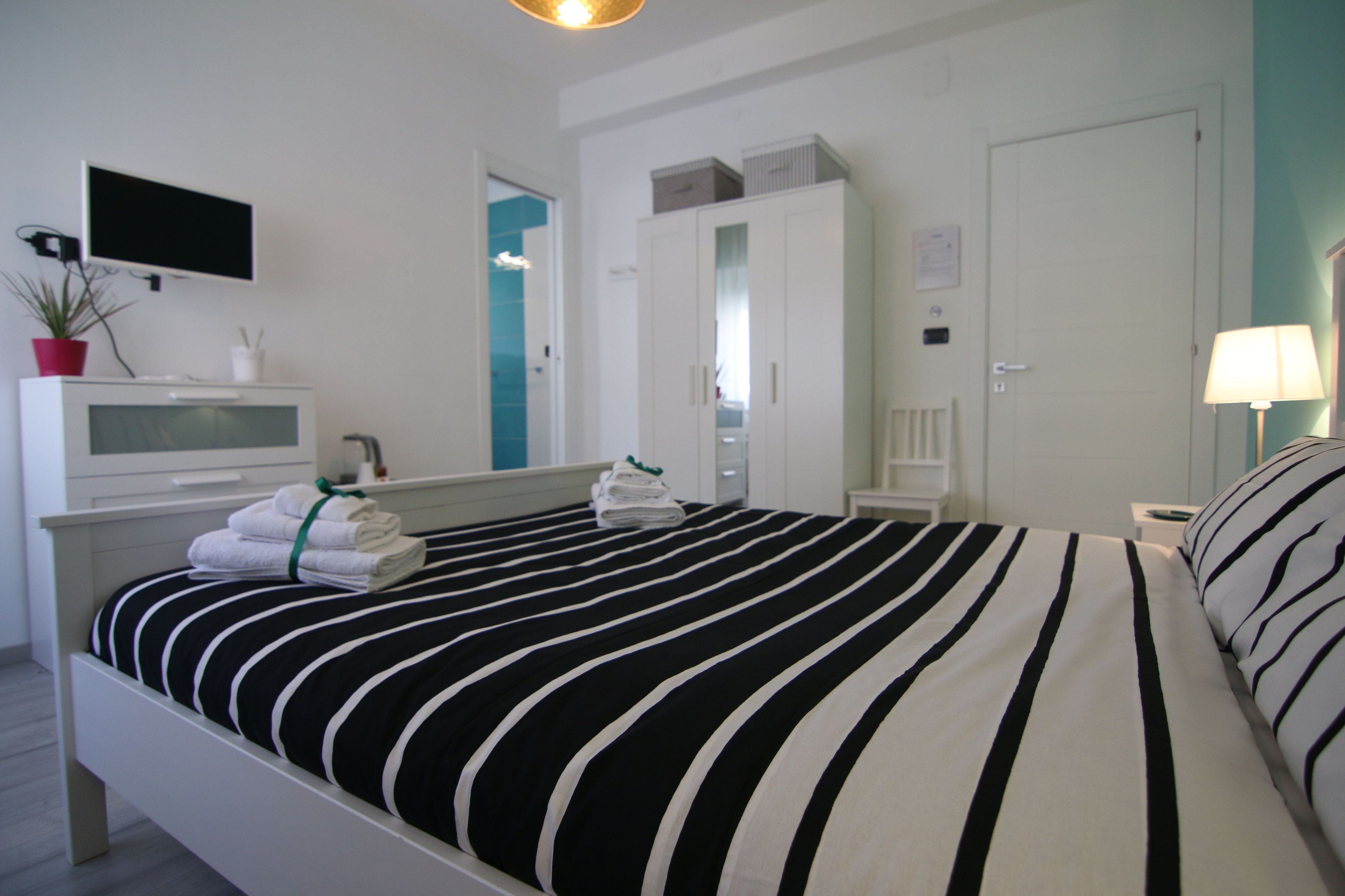 Habitación de hotel con cama, televisión, escritorio, silla, lámpara y planta en maceta.
