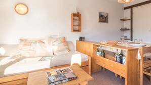 Un salon chaleureux avec un canapé, une table basse et une petite table en bois sur laquelle sont posées des bouteilles.