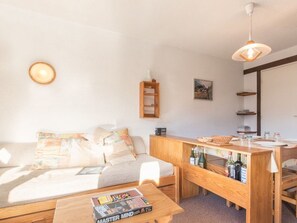 A cozy living room with a sofa, coffee table, and wooden side table with bottles. - Charming Studio in Serre-Chevalier with Balcony - Sleeps 4, WiFi, Dishwasher (Saint-Chaffrey)