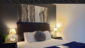 Une chambre d’hôtel moderne avec un grand lit, deux lampes de chevet, une horloge murale et un tableau au-dessus du lit.