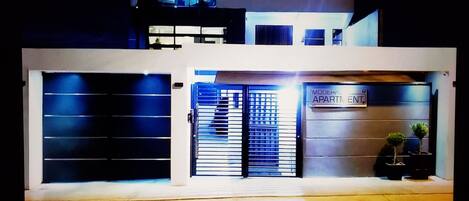 A modern building with a double garage door, a sign indicating 'Modern Apartment,' and a small potted plant on the ground.
