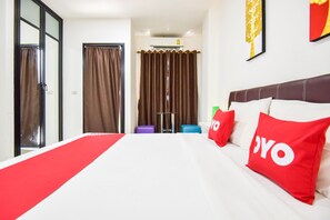 A hotel room with a large bed, red and white bedding, a red and white pillow, a brown curtain, and a wall-mounted air conditioner. - OYO 430 Tanya Place (Krabi)