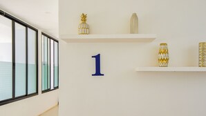 Un pasillo con un gran número azul, el '1', en la pared, puertas de vidrio y jarrones decorativos en estantes.