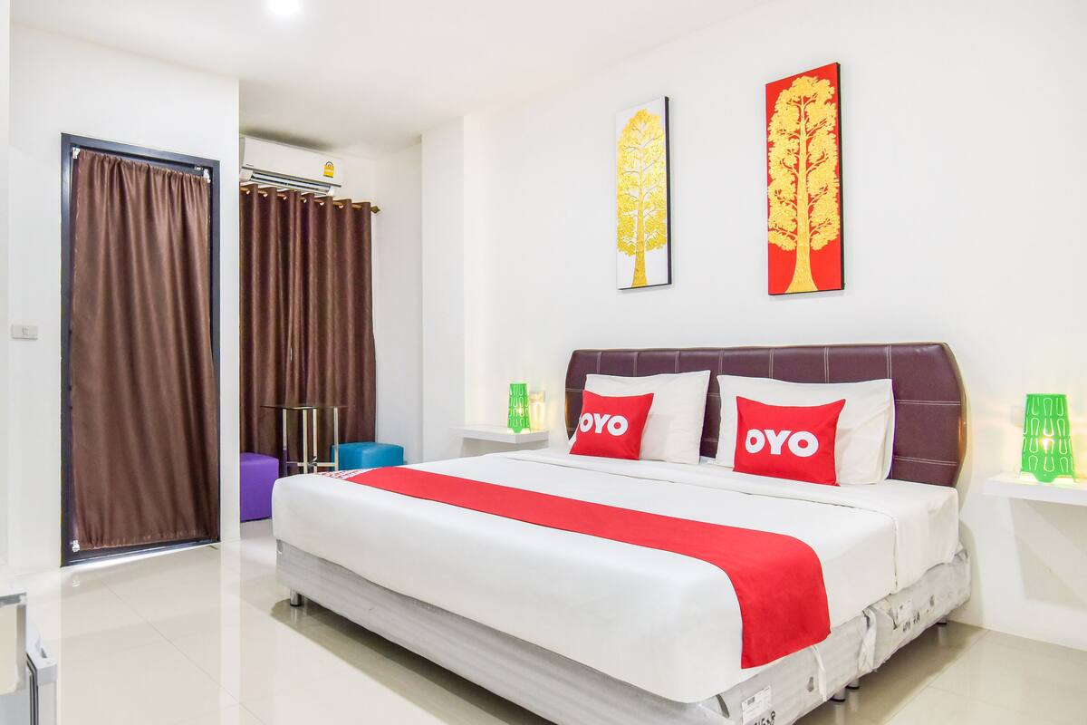 A hotel room with a large bed, two pillows with "OYO" branding, a red and white bedspread, and two wall art pieces of trees.