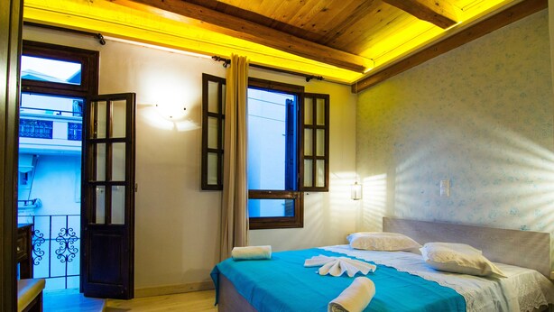 Ein Schlafzimmer mit Holzbalkendecke, einem Bett mit blauer Bettdecke, zwei weißen Kissen und einem aufgerollten Handtuch auf dem Bett.