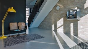A modern interior with a staircase, a bench, a yellow floor lamp, and a built-in TV. - Bett & Bude Boardinghouse (Sylt)