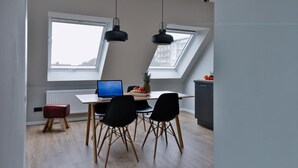A modern kitchen with a dining area, featuring a laptop, fruit bowl, and two pendant lights. - Bett & Bude Boardinghouse (Sylt)