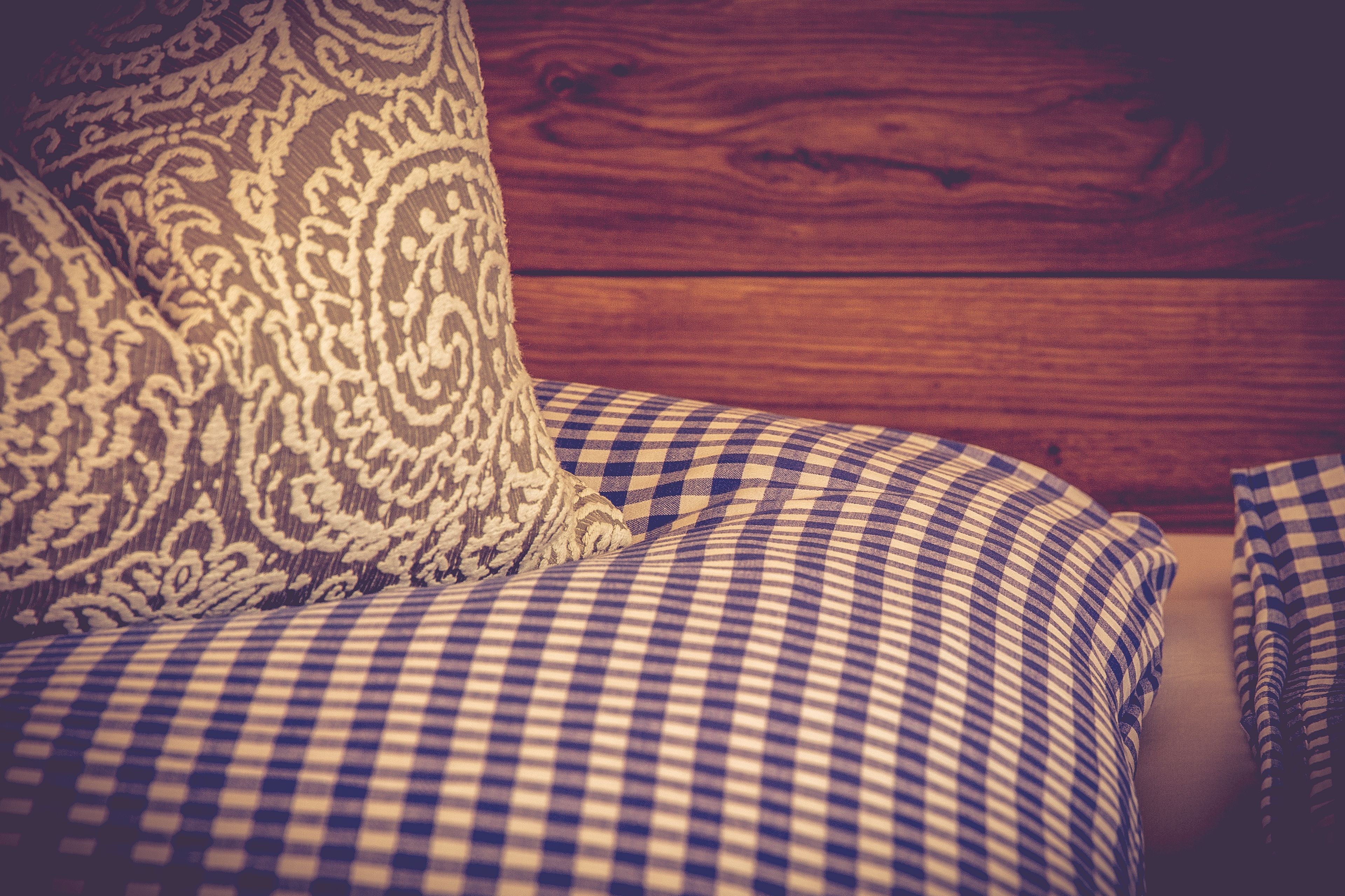A checkered sofa with a patterned pillow against a wooden wall.