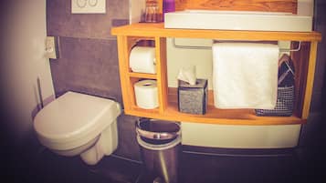 A compact bathroom with a toilet, a sink, and a small shelf with toiletries.