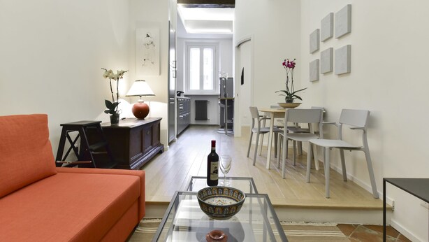 A modern living room with a sofa, a glass coffee table, and a dining area with chairs and a table.