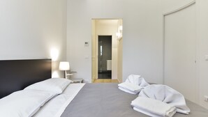 A hotel room with a bed, a nightstand, a lamp, and a bathroom visible through an open door.