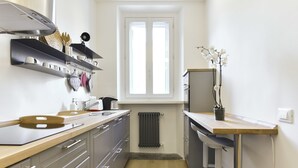 A modern kitchen with a wooden countertop, stainless steel appliances, and a window with blinds.