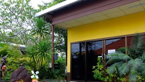 A building with a yellow facade, large glass doors, and a well-maintained garden with various tropical plants. - Sirimongkol Resort (Surat Thani)