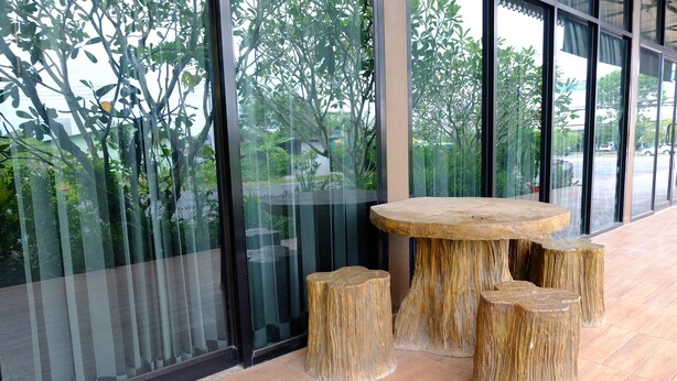 A modern interior with a round wooden table and matching stools, large windows with a view of greenery outside. - Sirimongkol Resort (Surat Thani)