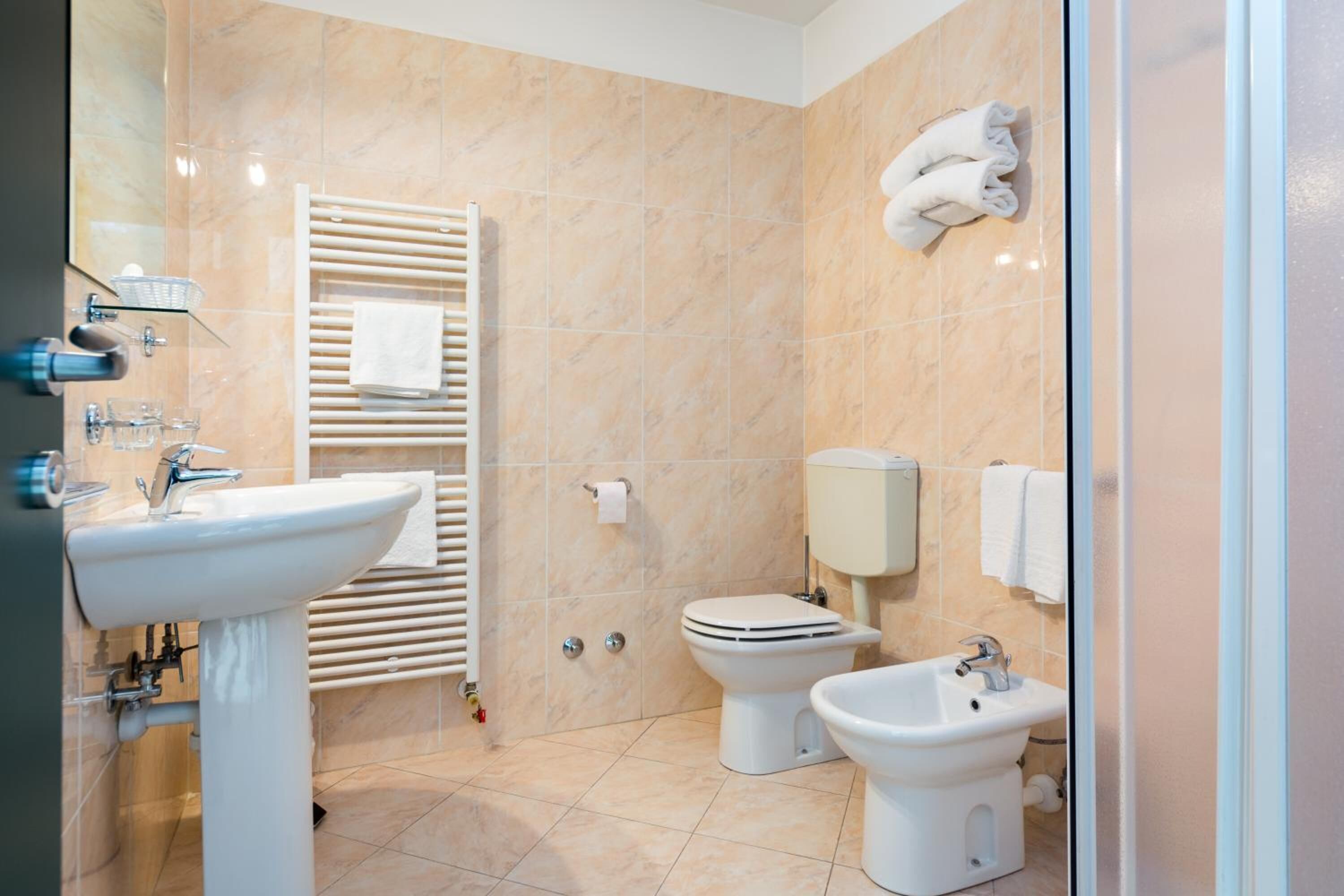 A bathroom with a sink, toilet, bidet, towel rack, and a glass shower enclosure.