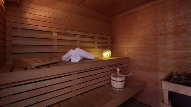 Una sauna de madera con bancos, un banco con toallas, un cubo de madera y una esfera decorativa.