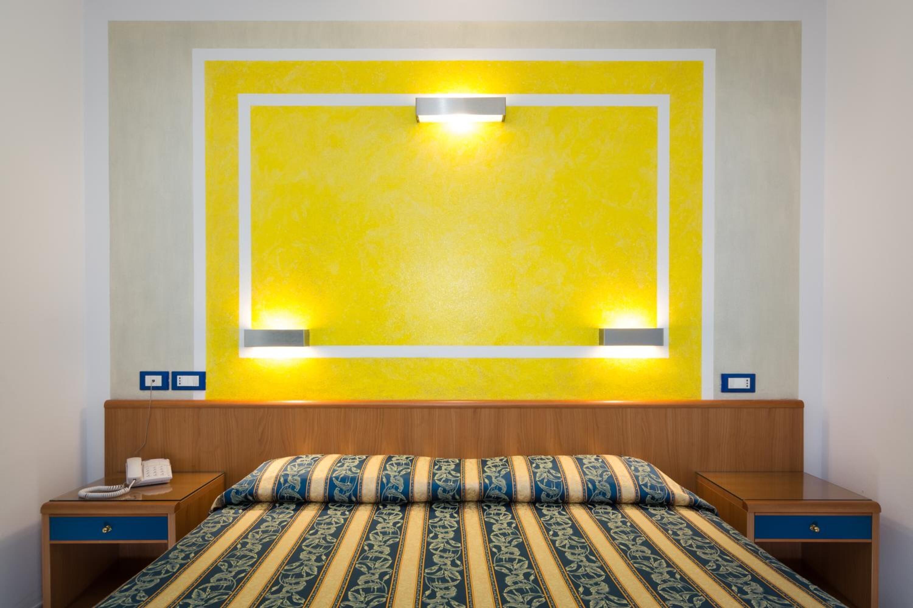 Een hotelkamer met een bed, nachtkastjes, een telefoon en een wandlamp.