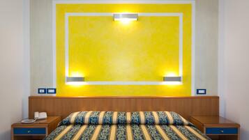Habitación de hotel con cama, mesitas de noche, teléfono y lámpara de pared.