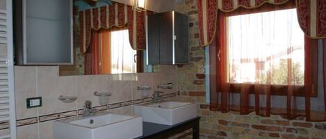 Casa de banho com duas pias, espelho e janela com cortinas.