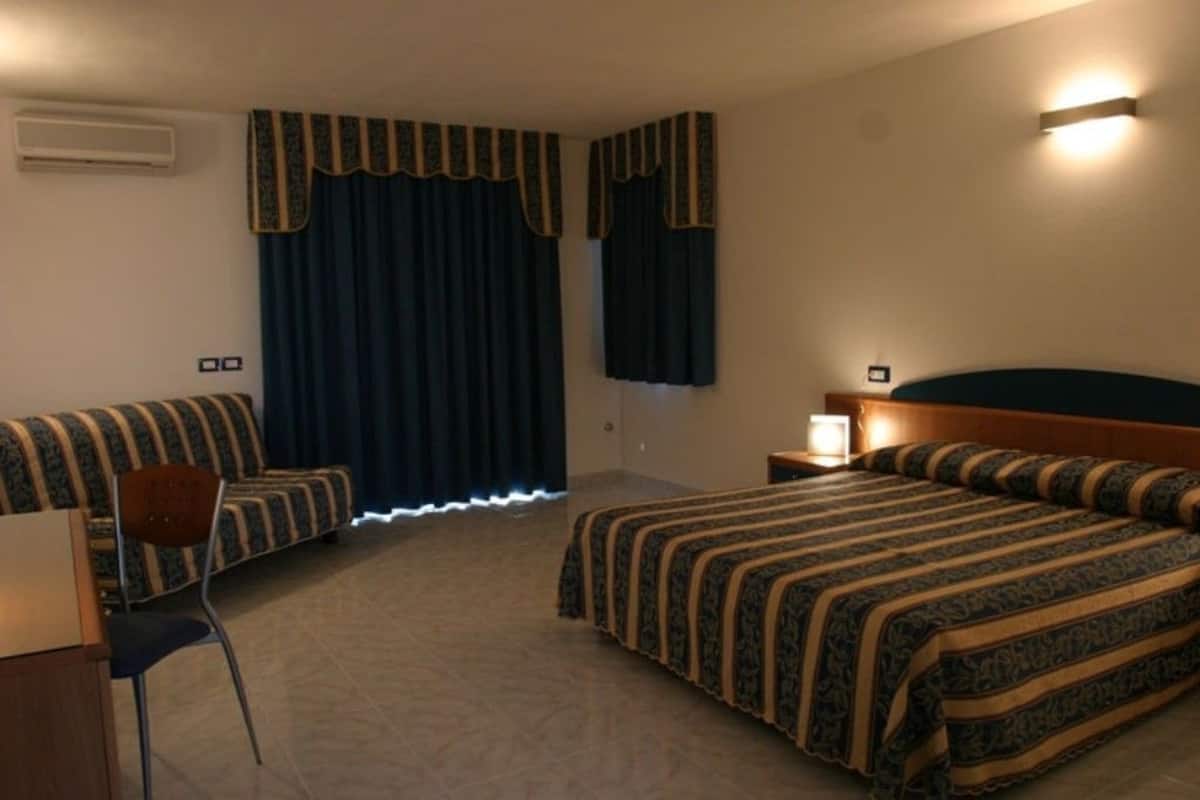 Una habitación de hotel con una cama, una silla, un escritorio y una mesita de noche.