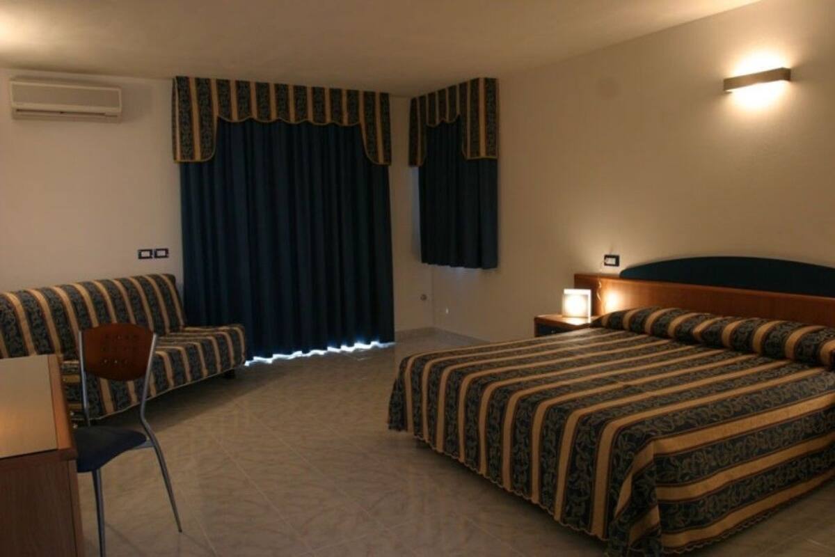 Una habitación de hotel con una cama, una silla, un escritorio y una mesita de noche.