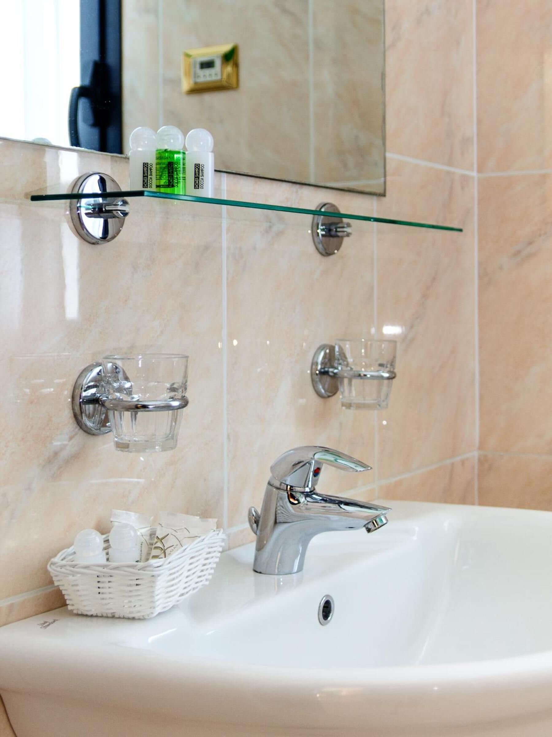 A bathroom with a white sink, chrome fixtures, and a glass shelf above the mirror.