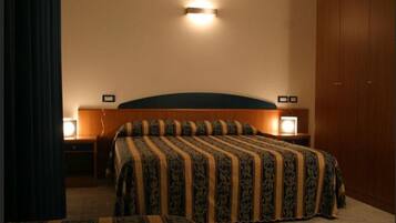 Quarto de hotel com uma cama grande, duas mesas de cabeceira com luminárias, cabeceira e um guarda-roupa.