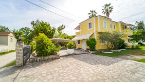 Una casa gialla con vialetto in pietra, circondata da vegetazione e palme.