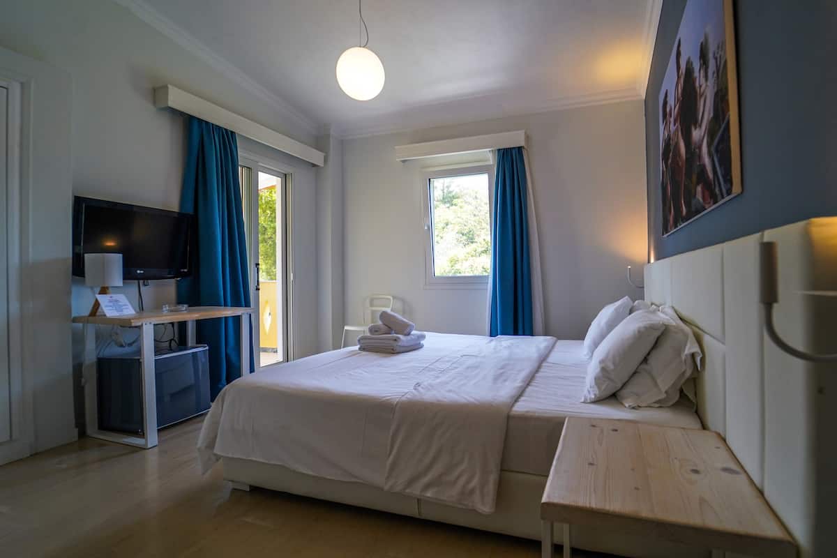 Une chambre à coucher avec un lit, une table de chevet, une télévision et une fenêtre avec des rideaux.